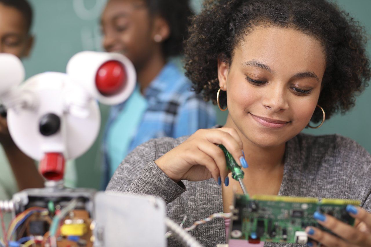 Uma menina com unhas pintadas de azul monta um robô em um laboratório de escola