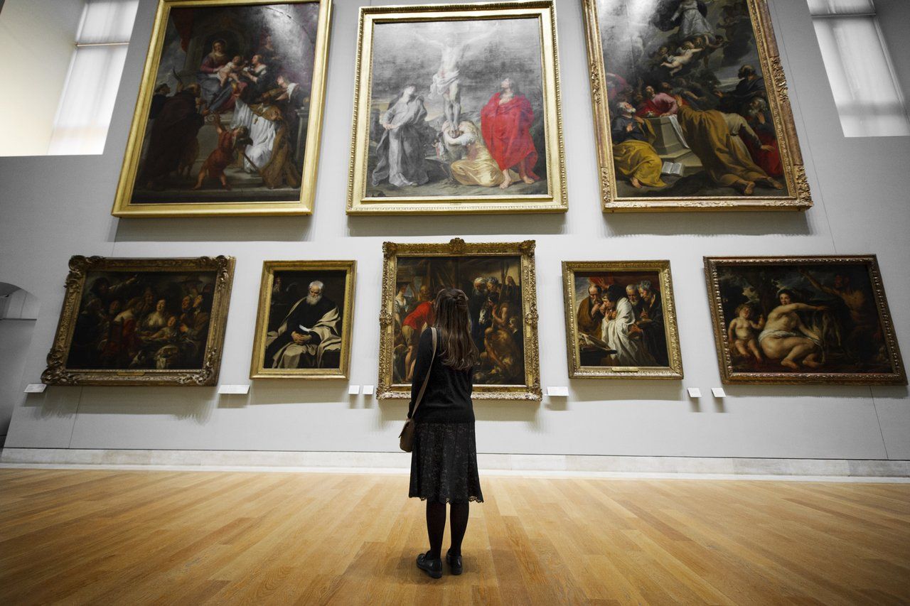 Visitante observa parede branca lotada de quadros em uma das salas do Museu do Louvre, em Paris, na França