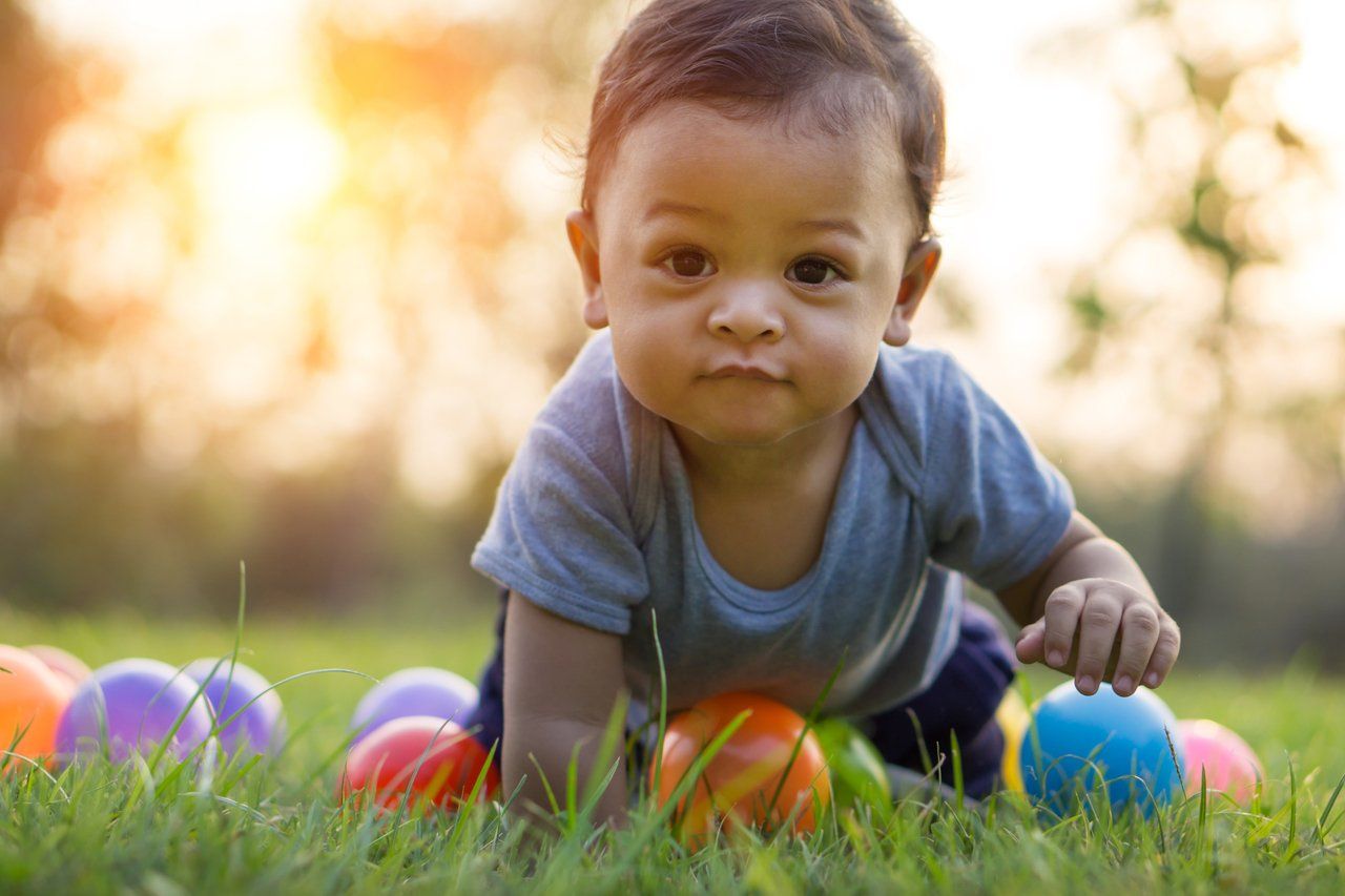 Bebê de bruços e olhando para a câmera, brinca na grama com bolas coloridas