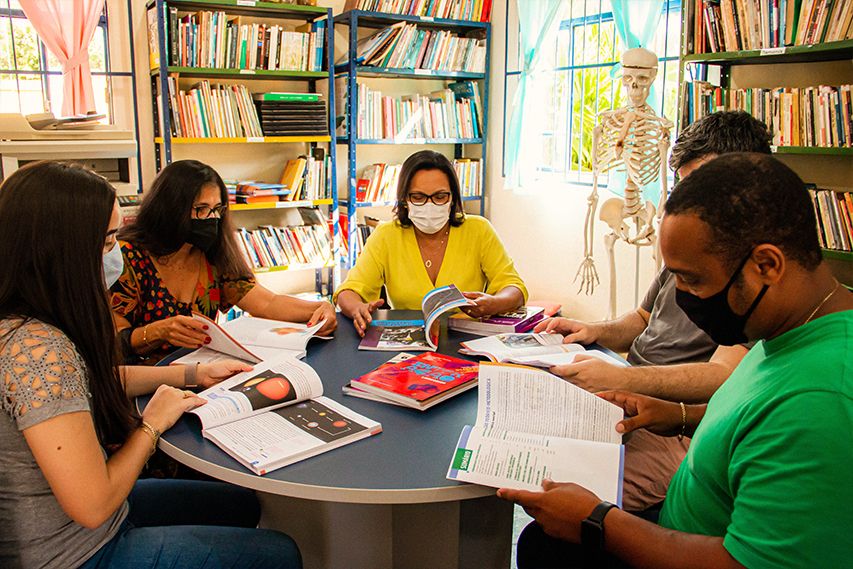 Equipe docente da EE Doutor Pompílio Guimarães, em Leopoldina (MG), sentados em uma mesa redonda no momento de planejamento.