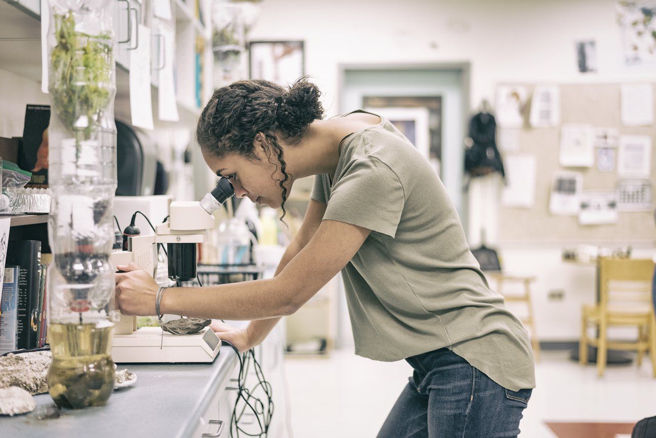 Adolescente do Ensino Médio analisa uma lâmina em um microscópio, em um laboratório de uma escola