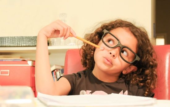 Menina de cabelos cacheados e óculos apoiando-se no lápis