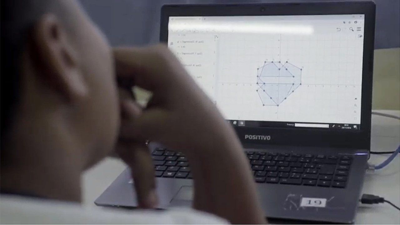 Aluno parado em frente a uma tela de computador que mostra uma figura geométrica