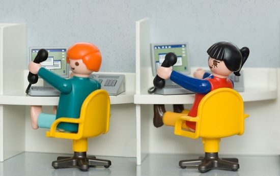 Dois bonecos de brinquedo, um masculino e um feminino, simulam um escritório de telemarketing, falando ao telefone enquanto usam o computador