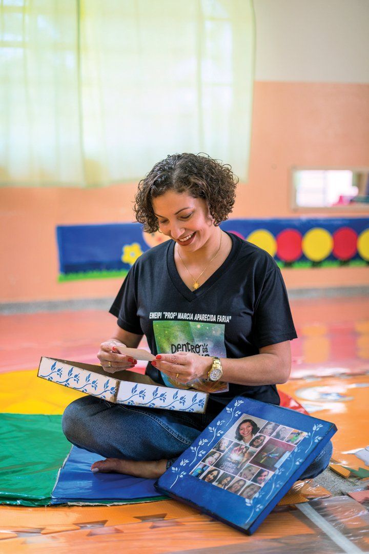 Coordenadora Pedagógica Karina, sentada de pernas cruzadas, lança um olhar carinhoso para uma das fotos de sua infância que trouxe para compartilhar com os professores.