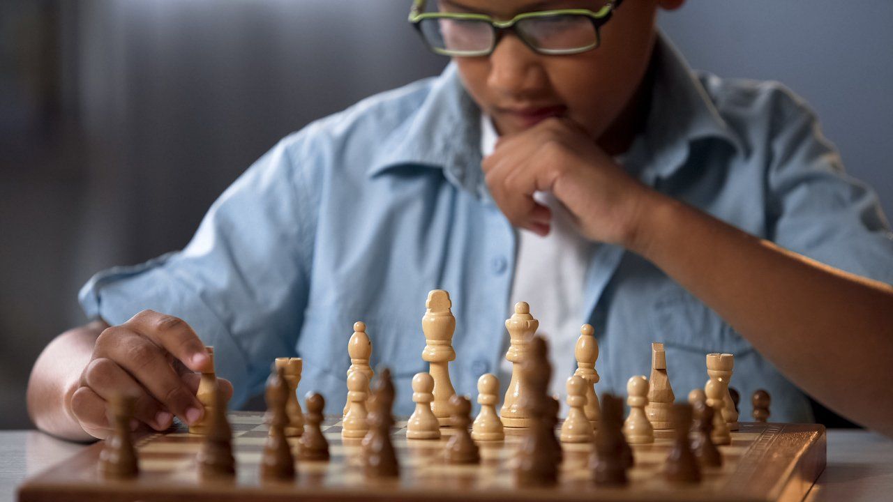 Estudante pensa diante de um tabuleiro de xadrez
