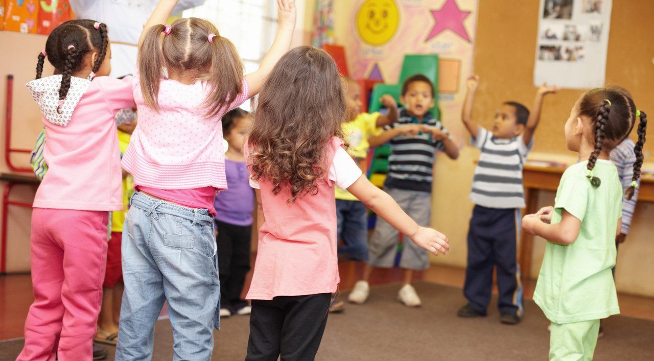 Crianças reunidas em uma roda dançam e cantam em sala de aula